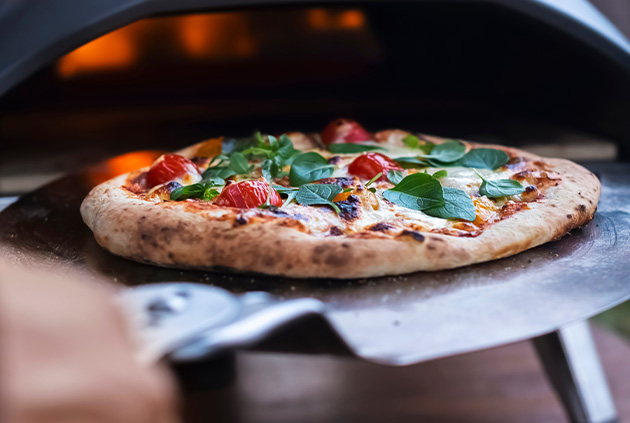 Wood fired pizza oven in outdoor kitchen being taken out on stainless steel pizza lifter.